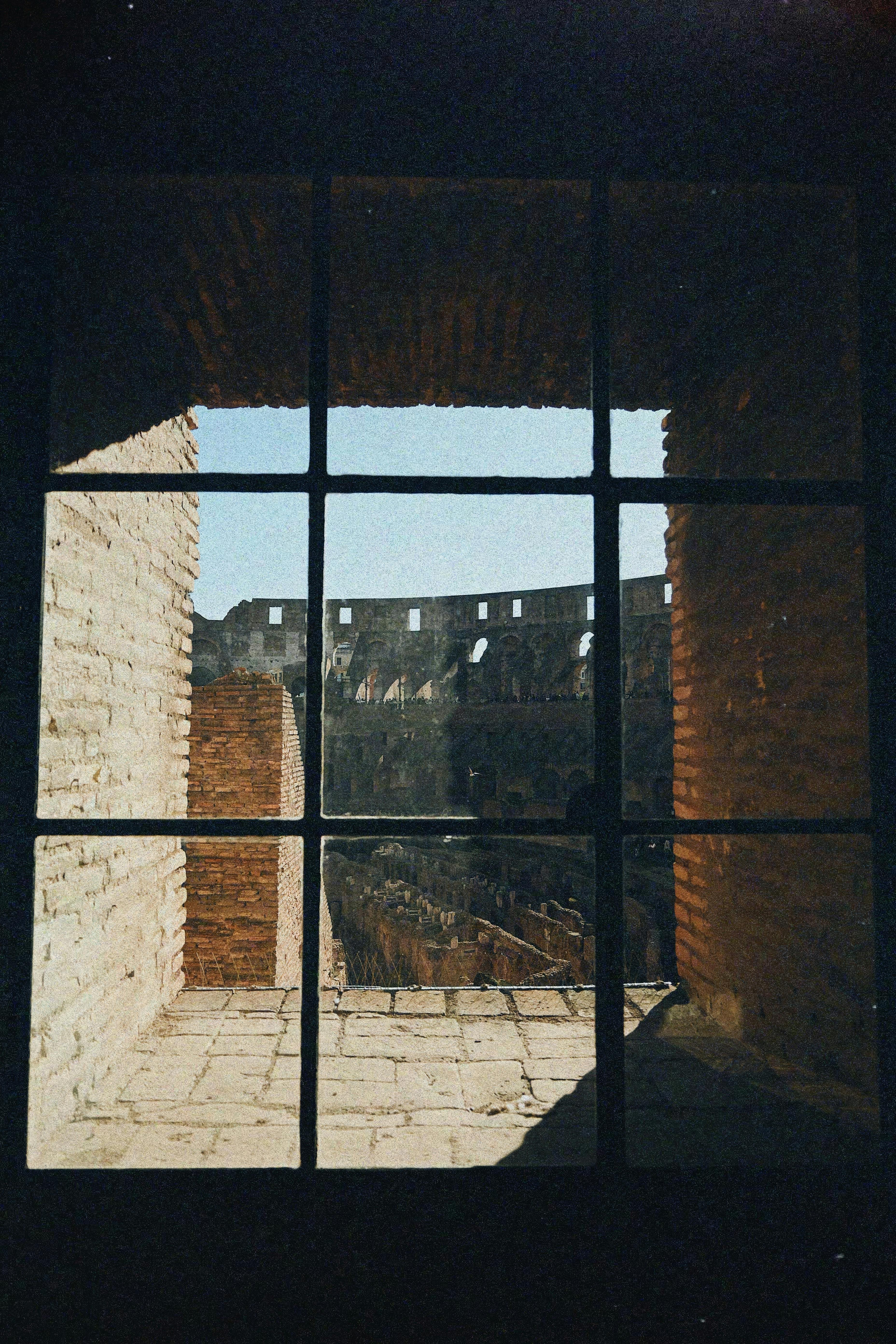 A scenic view of the Colosseum in Rome seen through a rustic brick window.