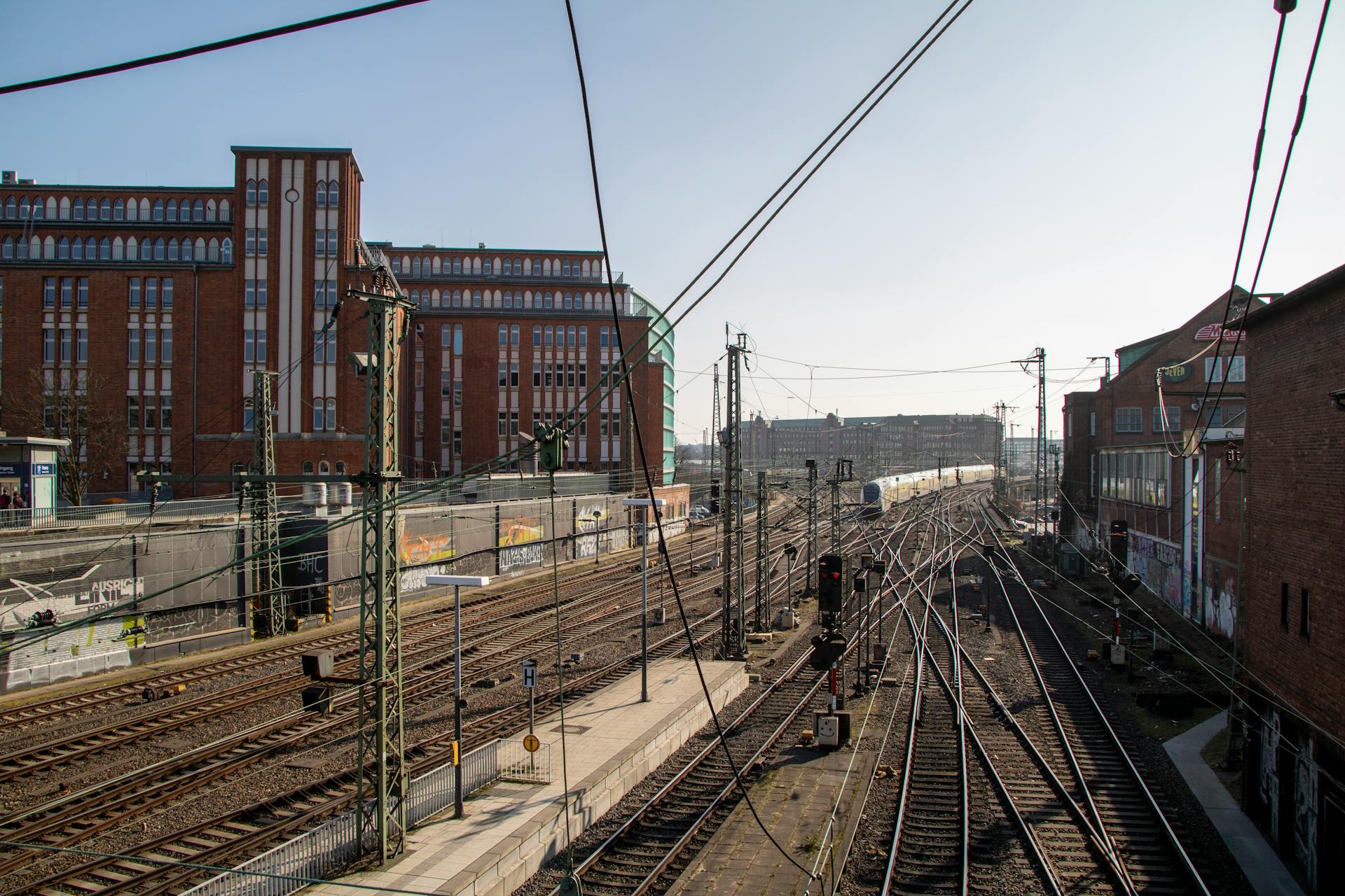 Railroad tracks in Hamburg under a clear blue sky with industrial buildings.