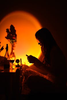 Silhouette of woman on phone, warm ambient light, cozy atmosphere.