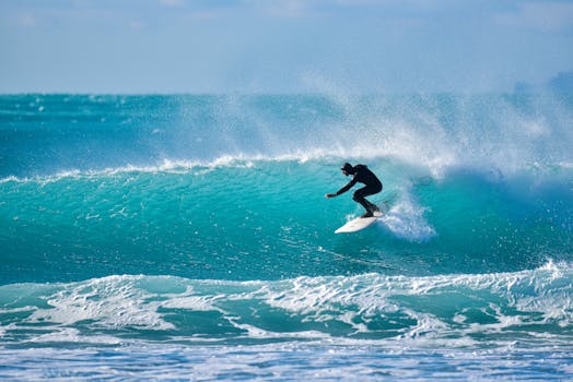 Thrilling shot of a surfer riding a vibrant turquoise wave under the bright sky.