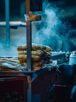 Freshly grilled corn on the cob stacked at a bustling night market food stall.