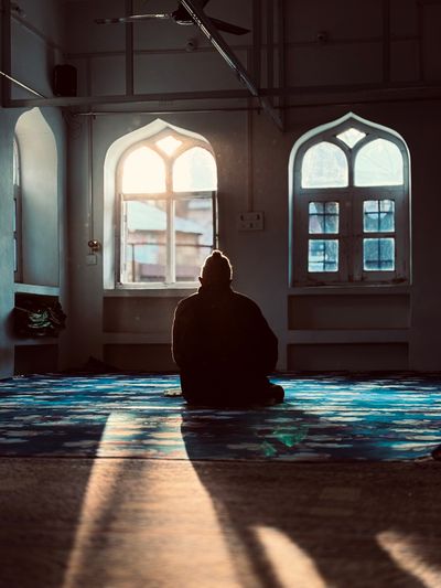A person sits in quiet prayer in a modest prayer room with arched windows