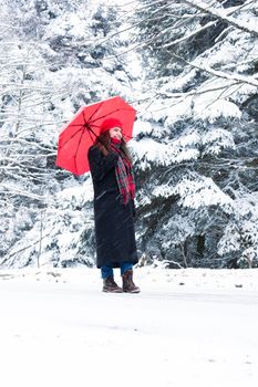 Woman in winter clothing walking with red umbrella amidst snow-covered trees, conveying seasonal joy.