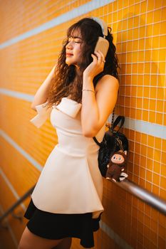 一位时尚的年轻女子在色彩鲜艳的瓷砖墙边戴着耳机听音乐。 - 相关推荐
