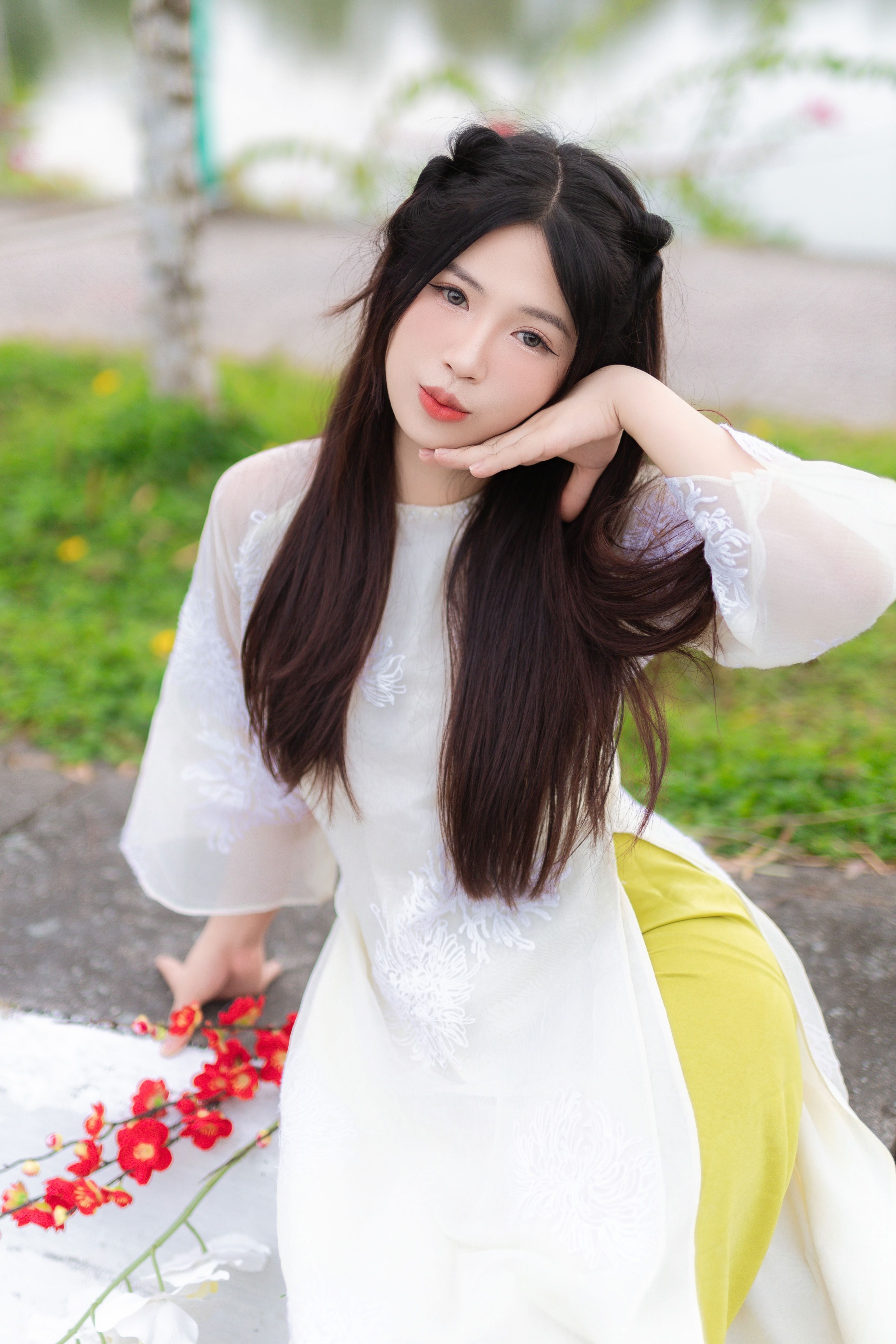 Young woman posing in a white dress with flowers outdoors, exuding elegance.