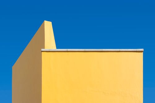 Free A minimalist architectural shot of a yellow wall contrasted with a clear blue sky. Stock Photo