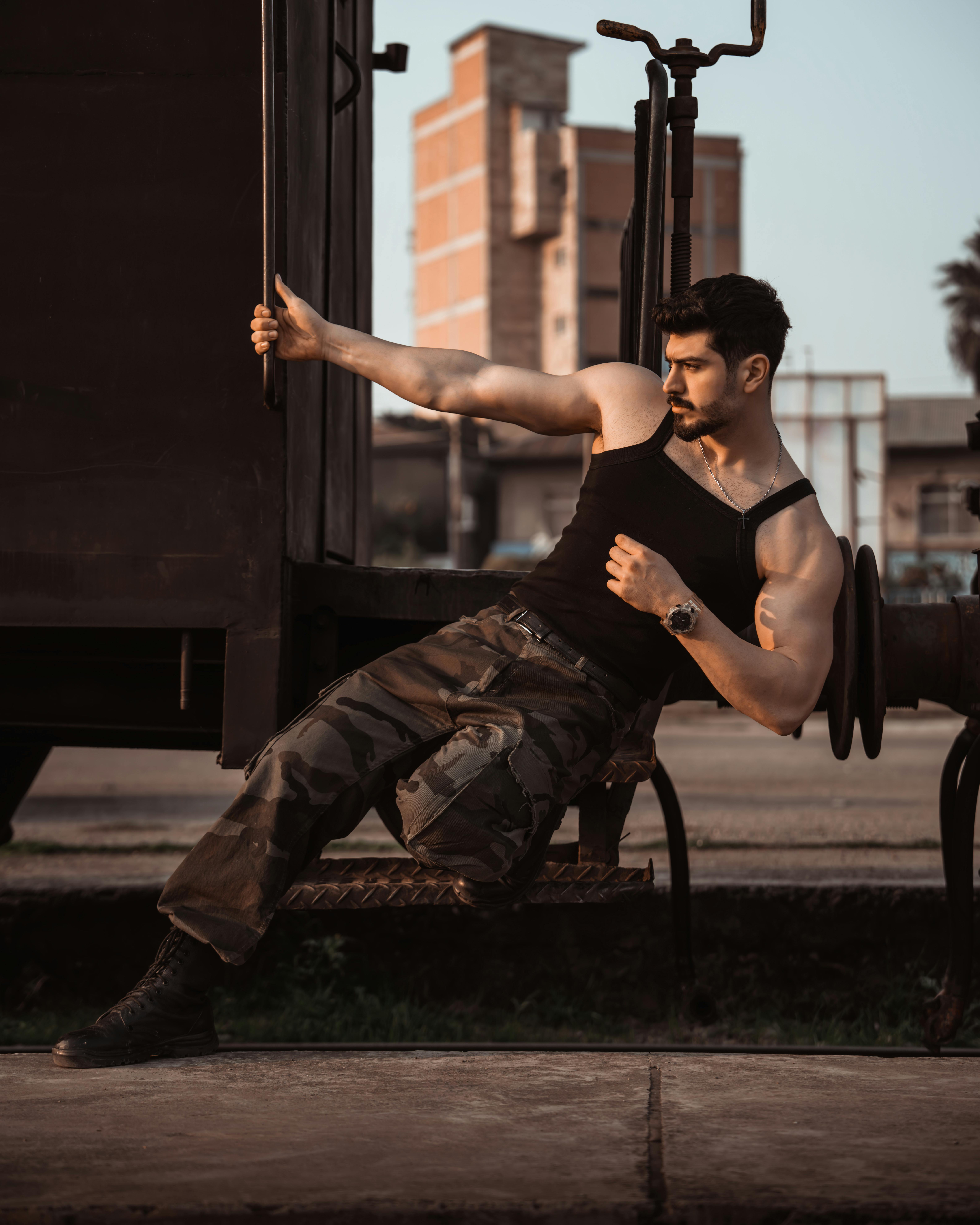 Man posing outdoors in urban environment wearing military-style pants.