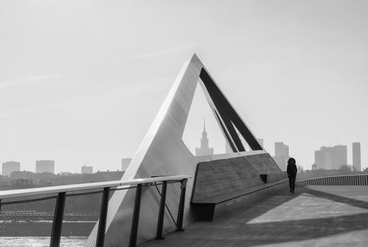 Black and white image of a modern triangular structure with Warsaw skyline in the background.