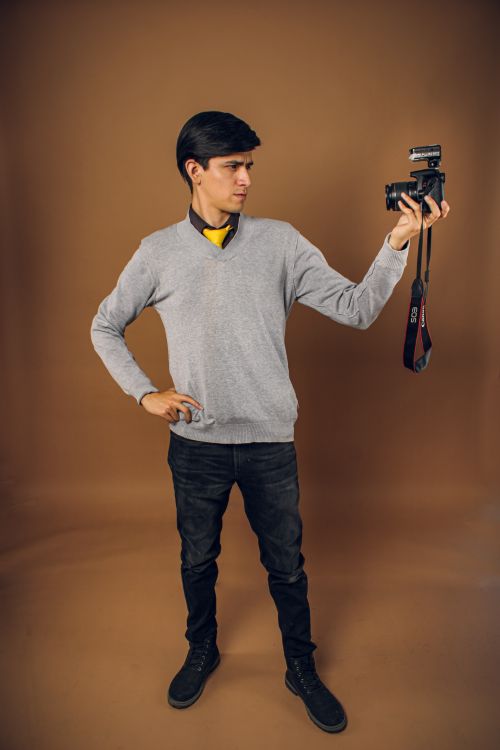 Free Man in casual attire holding a camera against a brown studio background. Stock Photo