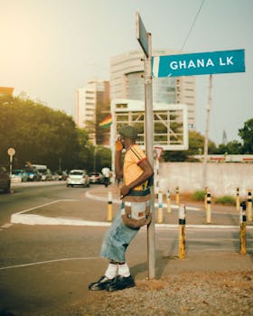A young adult on a city street in Kumasi, Ghana, with an urban background and signage.