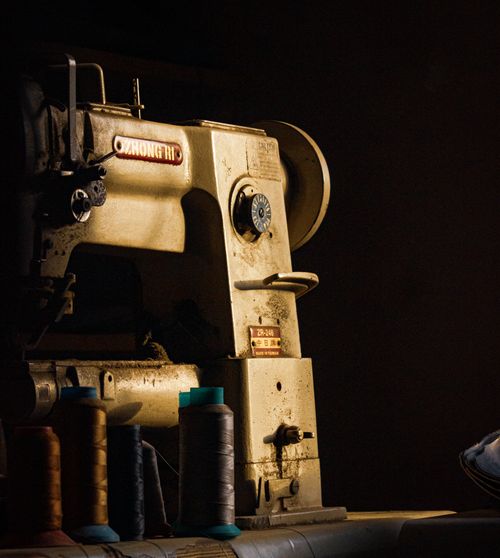 Free A vintage sewing machine with spools of colorful threads in a dimly lit setting. Stock Photo