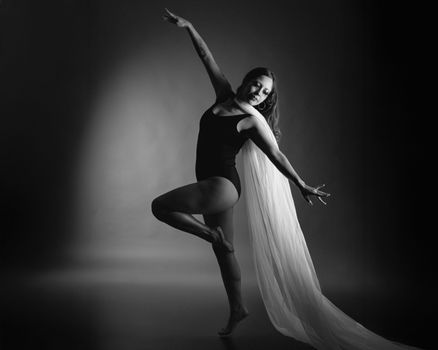 A graceful ballerina performing in a black leotard with flowing fabric in monochrome.