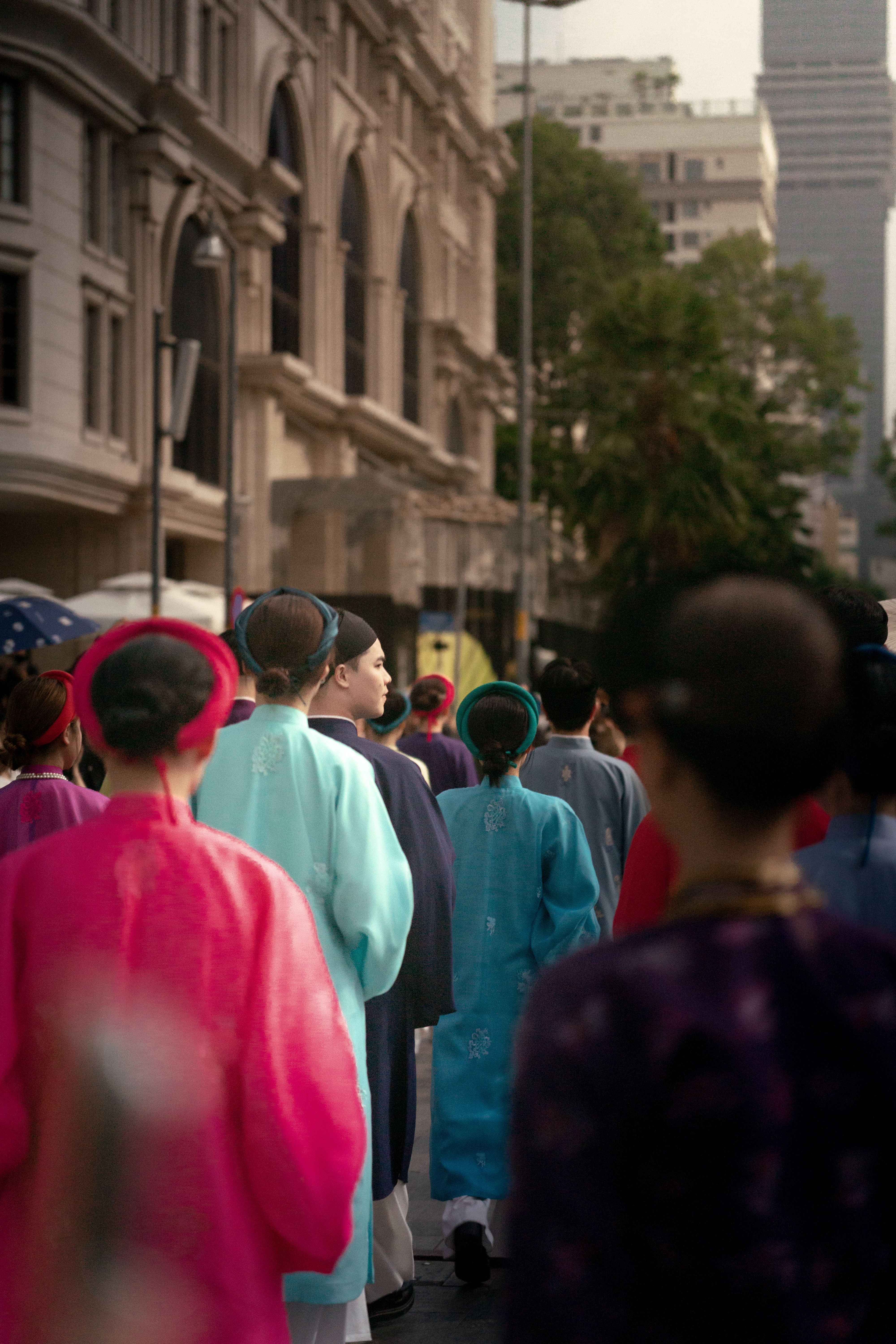 A group of people wearing colorful traditional Asian garments walking in a city parade.