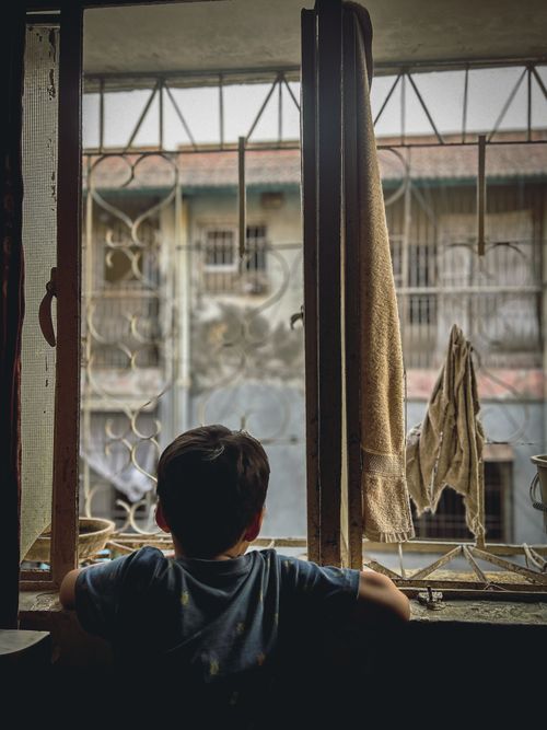 Free A young child looks pensively out of a window in Karachi, Pakistan, showcasing urban life's simplicity. Stock Photo
