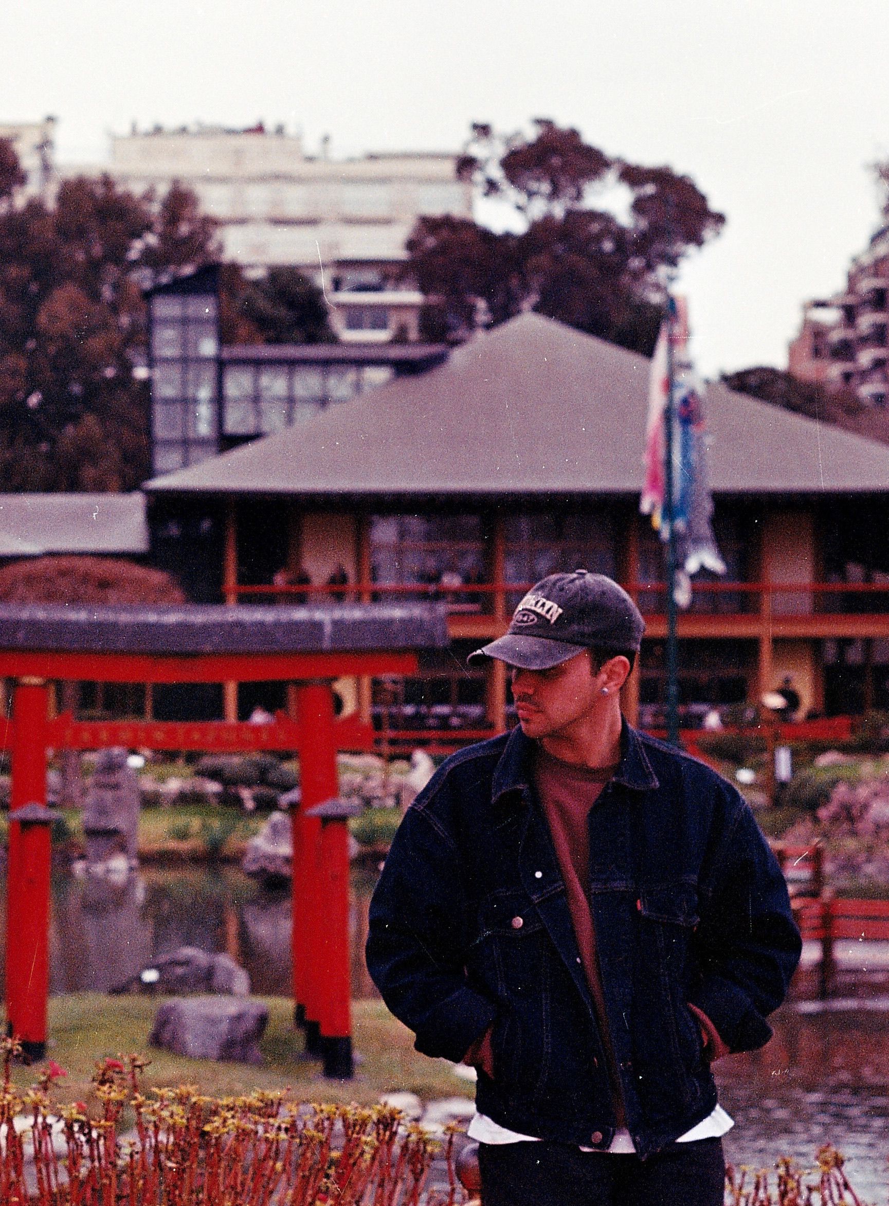 Young man in a Japanese garden with traditional red Torii gate and cultural flags.