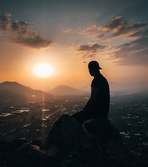 Free Man Sitting on Rock During Golden Hour Stock Photo