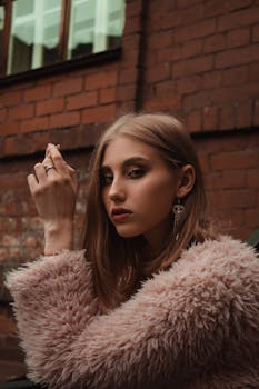 Young woman in a pink faux fur coat posing stylishly against a brick wall.