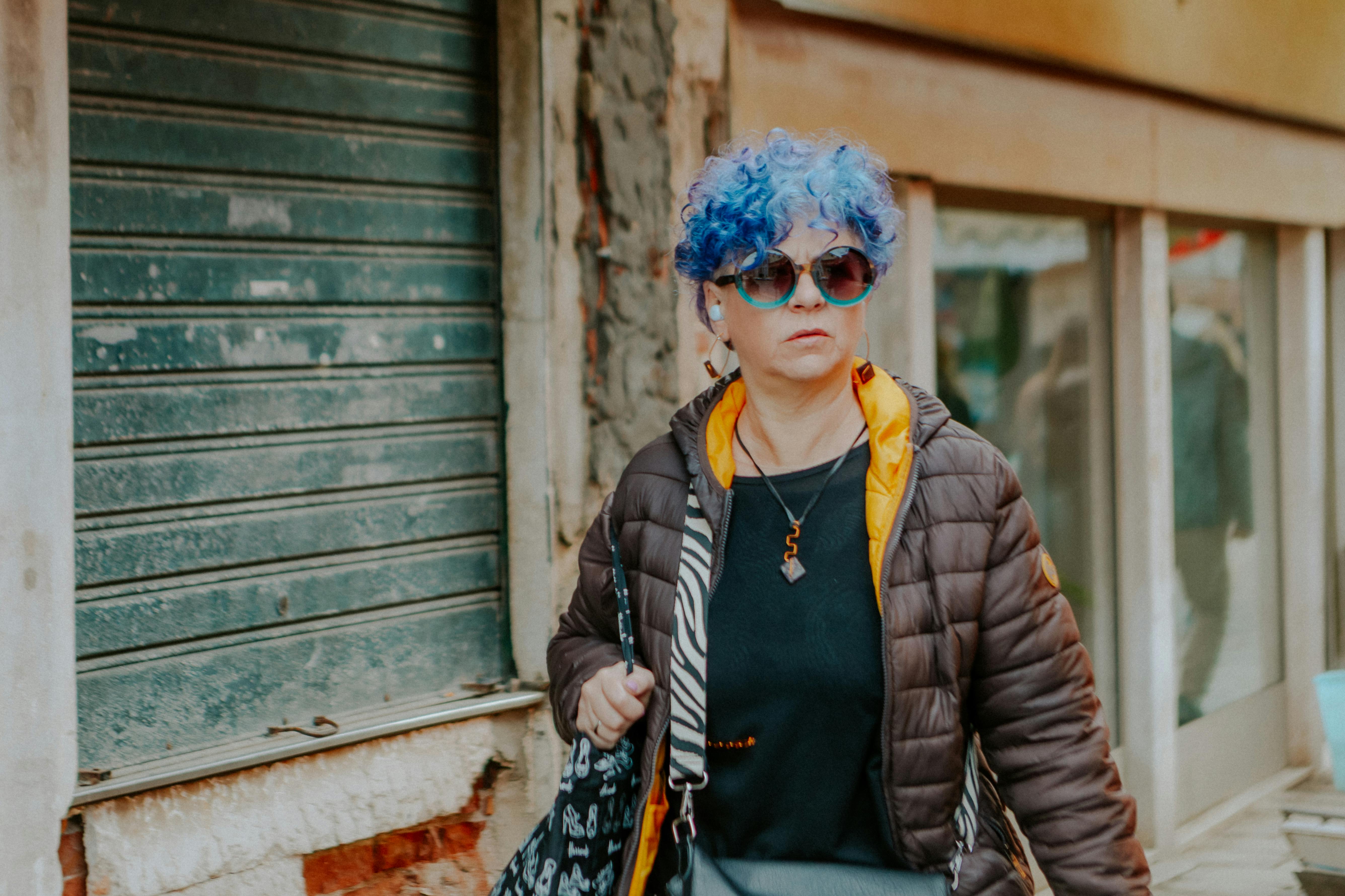 Woman with vibrant blue hair and sunglasses walking outdoors, showcasing unique fashion style.