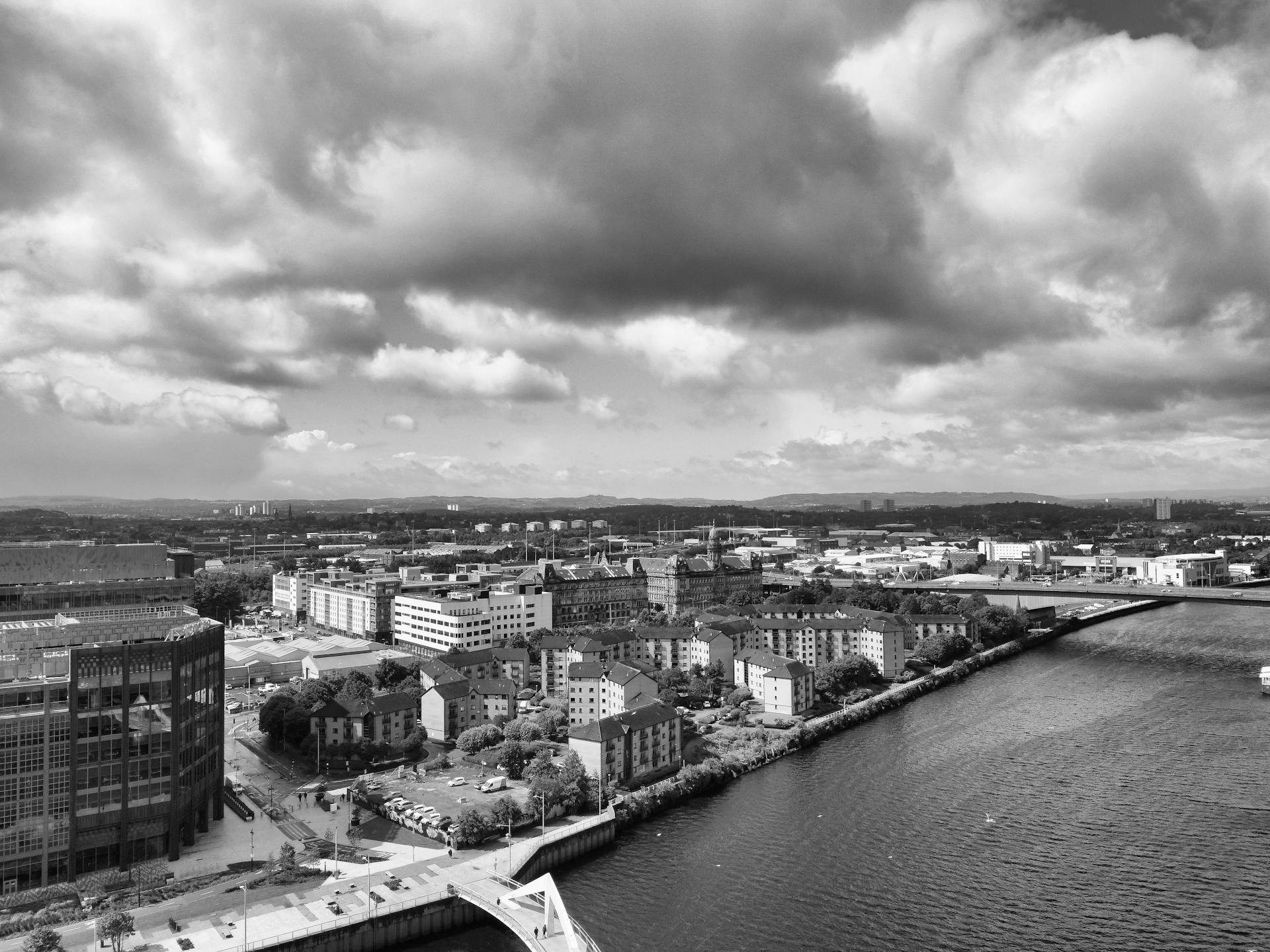 Black and white aerial view of Glasgow cityscape with dramatic clouds overhead, featuring river and buildings.