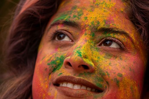 Colorful close-up portrait of a woman celebrating Holi with vibrant powder on her face.