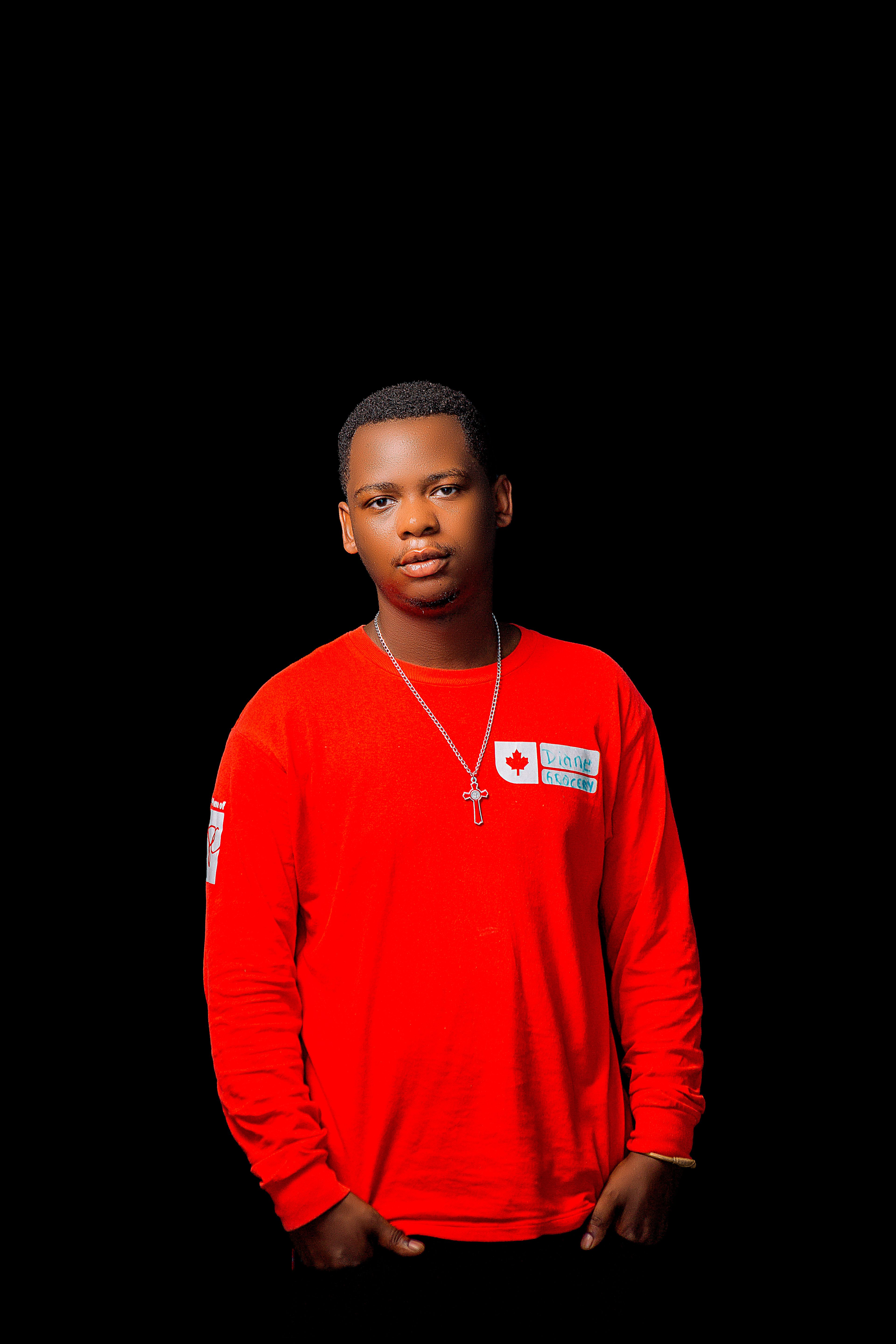 Portrait of a young man wearing a red shirt with a silver cross necklace on black background.
