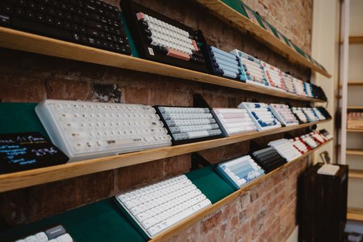A variety of mechanical keyboards neatly displayed on a shelf in a brick-walled store interior.