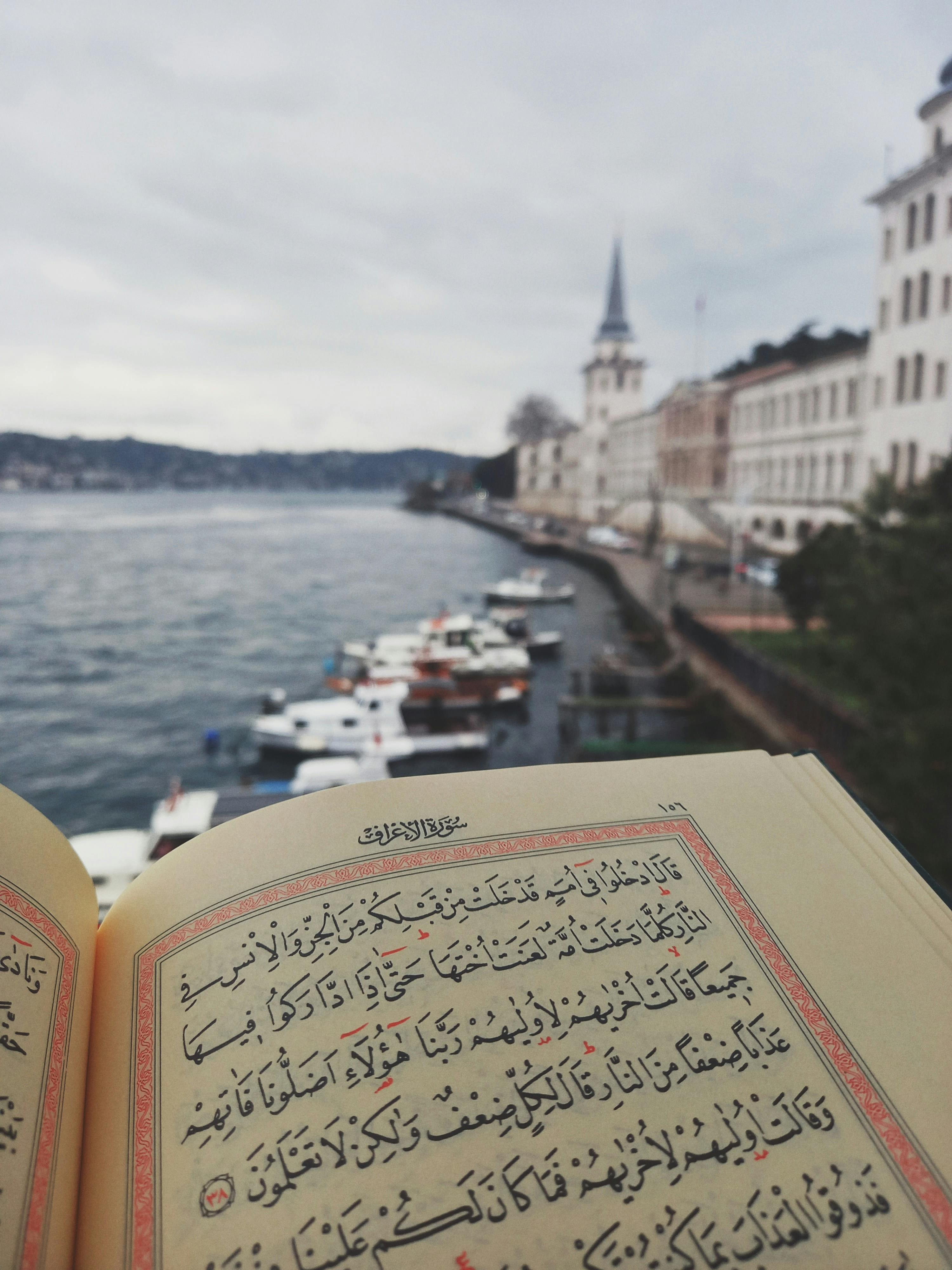 Open Quran with Arabic script overlooking a calm waterfront in Istanbul cityscape.