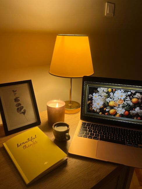 Warm evening setup with a laptop, lamp, coffee cup, notebook, and candle for relaxation.