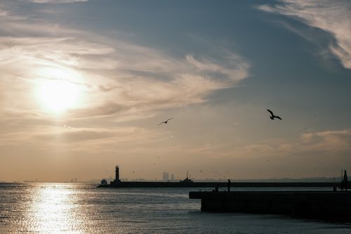 Free Peaceful evening seascape with a glowing sunset and lighthouse silhouette. Stock Photo