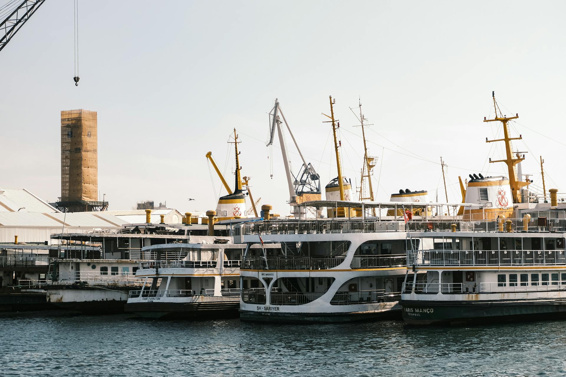 Passenger ferries docked at an industrial port with visible cranes and maritime infrastructure.