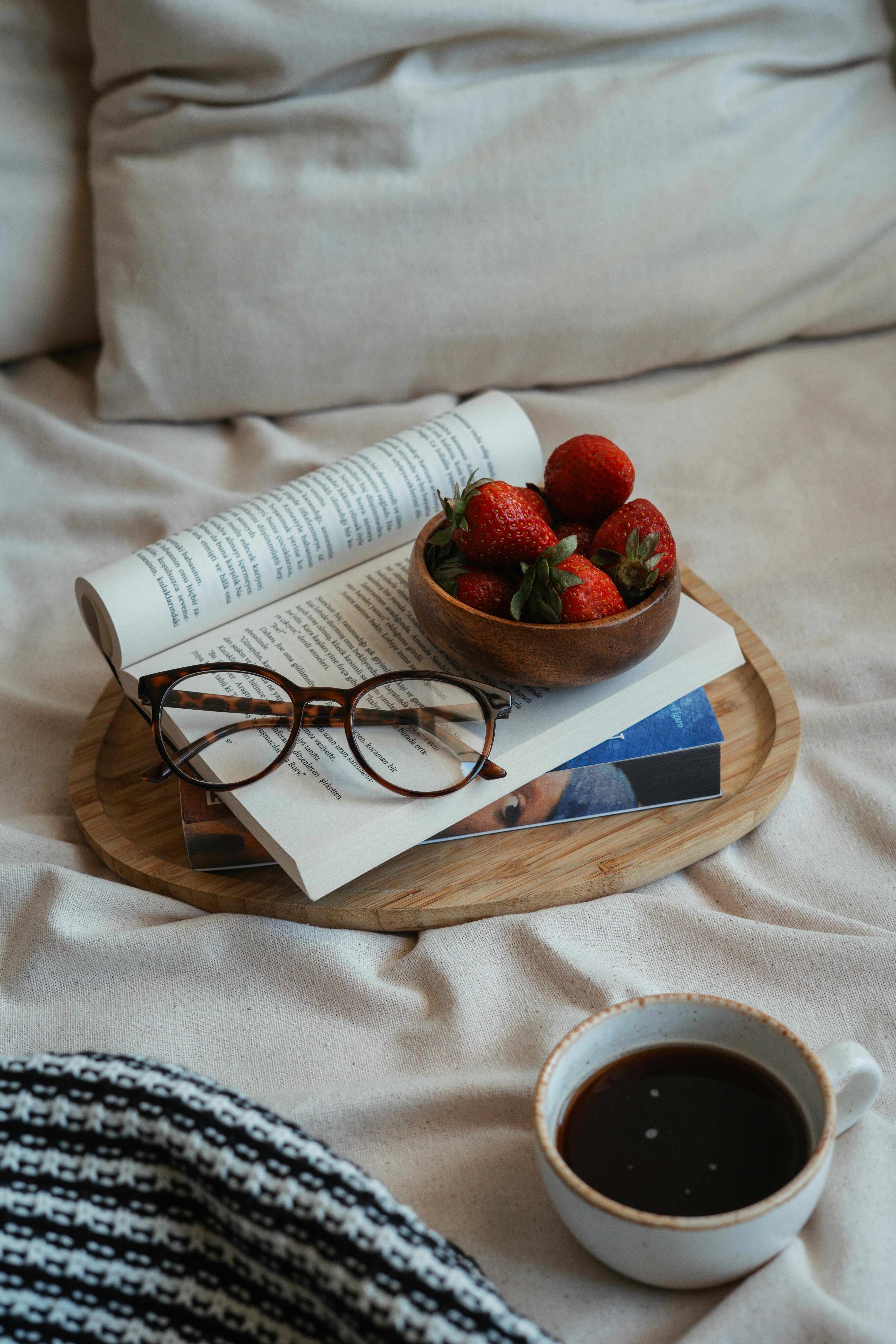 A warm, inviting setup with strawberries, coffee, and books on a bed.