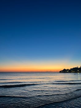 Tranquil beach scene at sunrise with vibrant sky and calm waves.