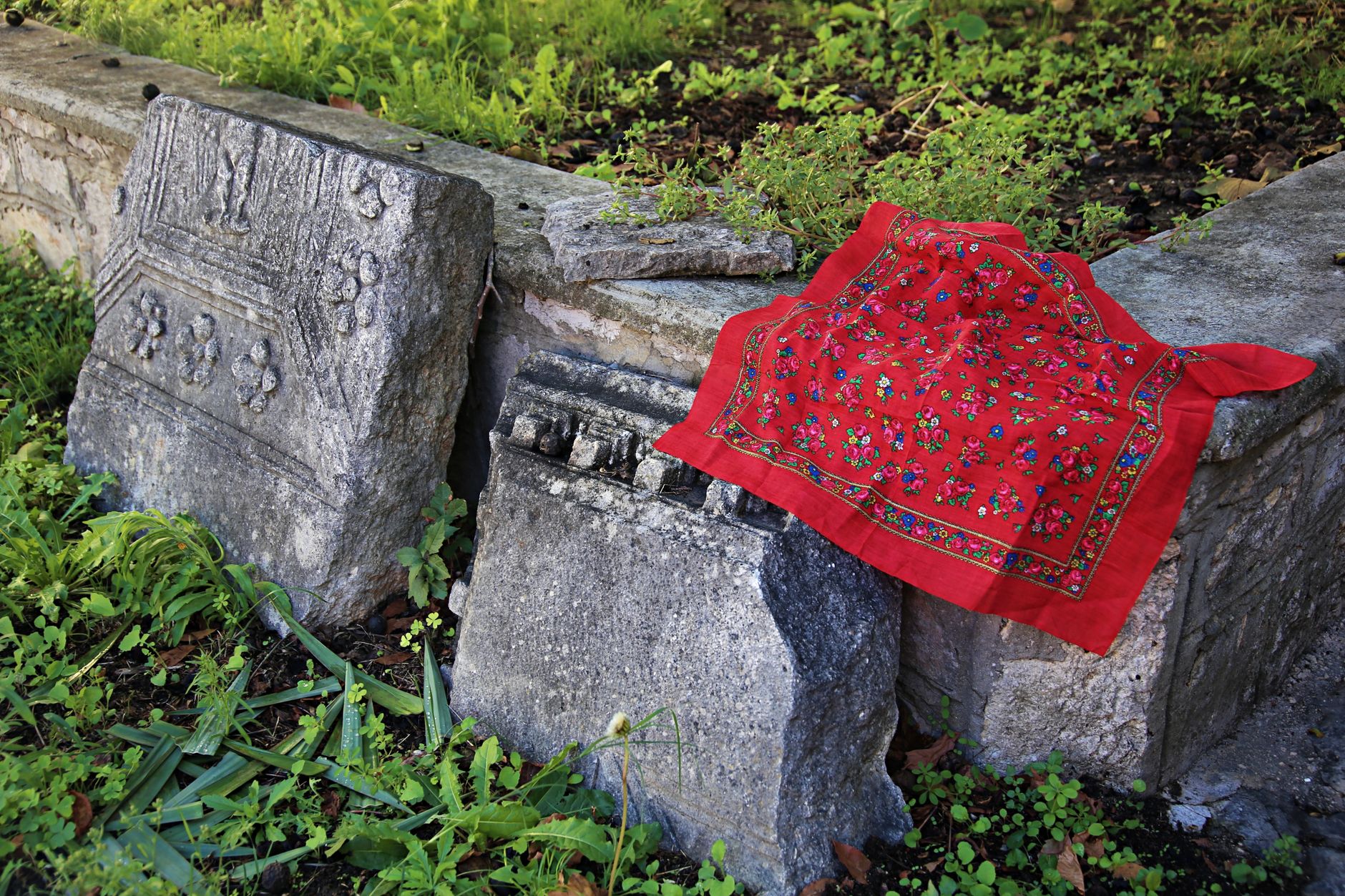 Historic stone relics adorned with a colorful red cloth in a lush garden setting.