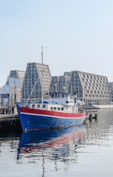A vibrant boat docked near modern buildings at Copenhagen's waterfront.