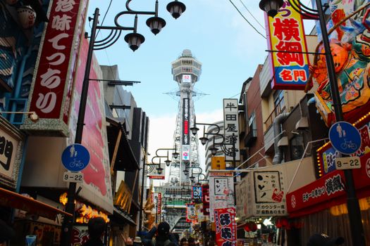 Vibrant street scene in Osaka with the iconic Tsutenkaku Tower and bustling shops.