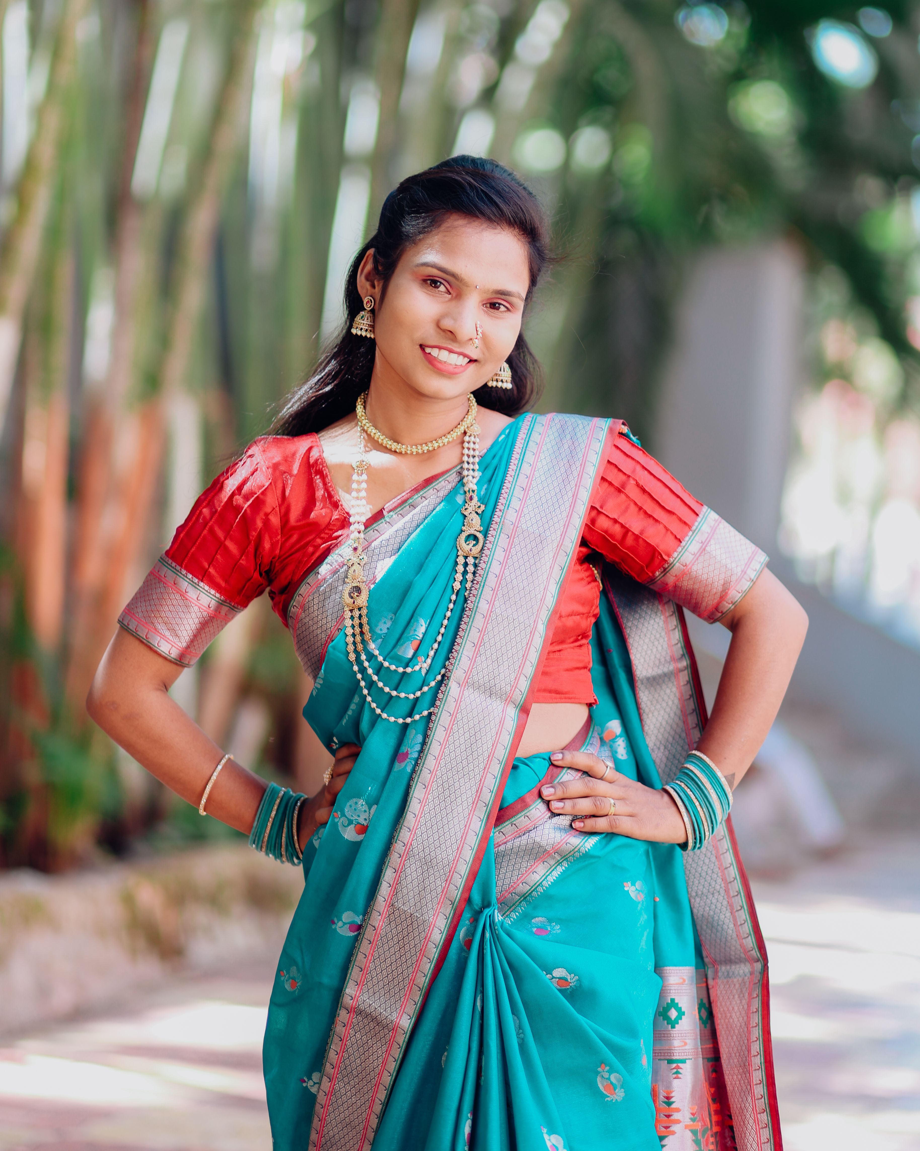 A woman in vibrant traditional Indian attire posing outdoors with graceful jewelry.