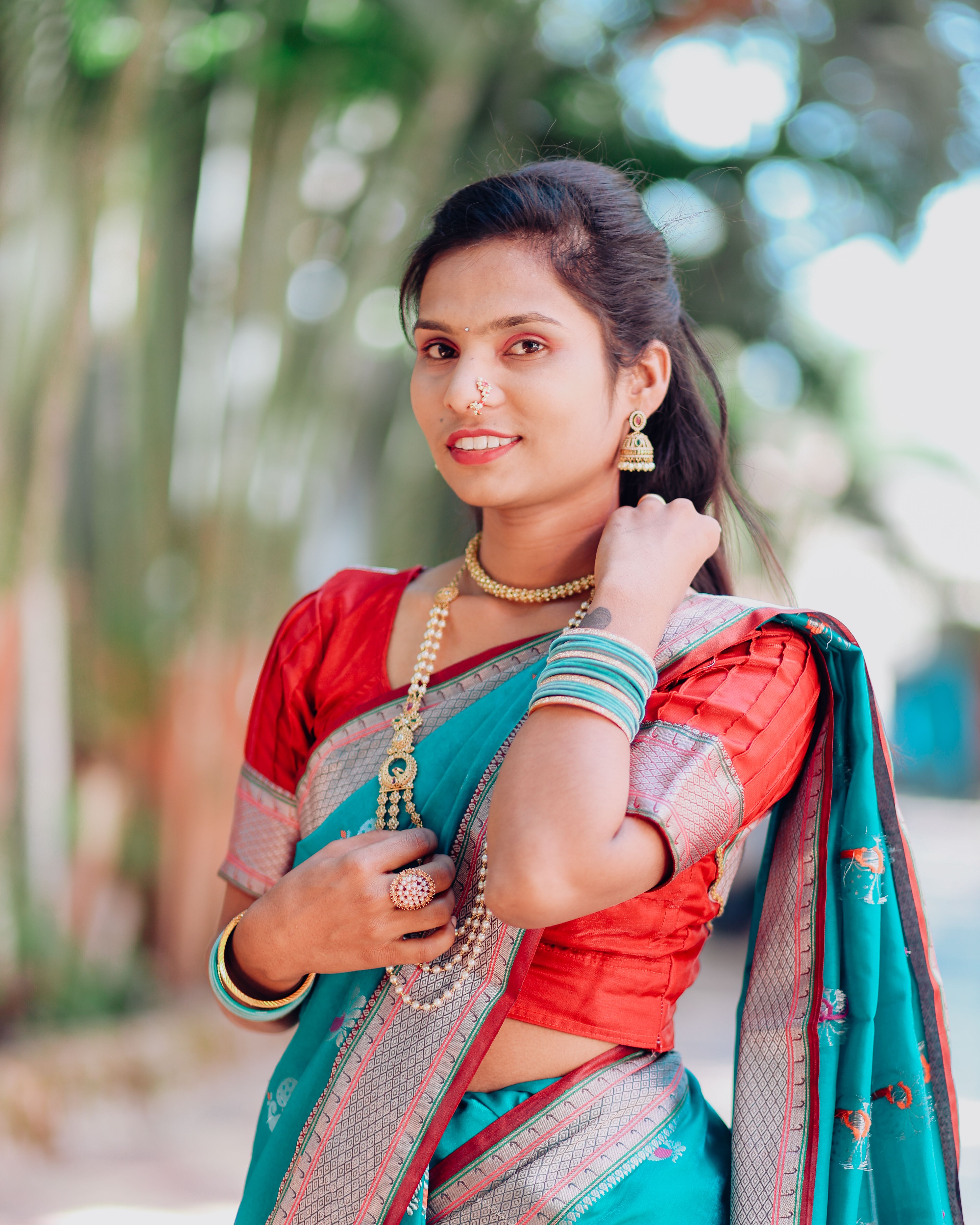 Portrait of a smiling woman in traditional Indian saree with jewelry, outdoors with blurred background.