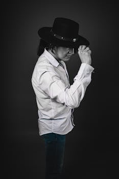 Profile portrait of a man in a cowboy hat and white shirt against a dark backdrop.