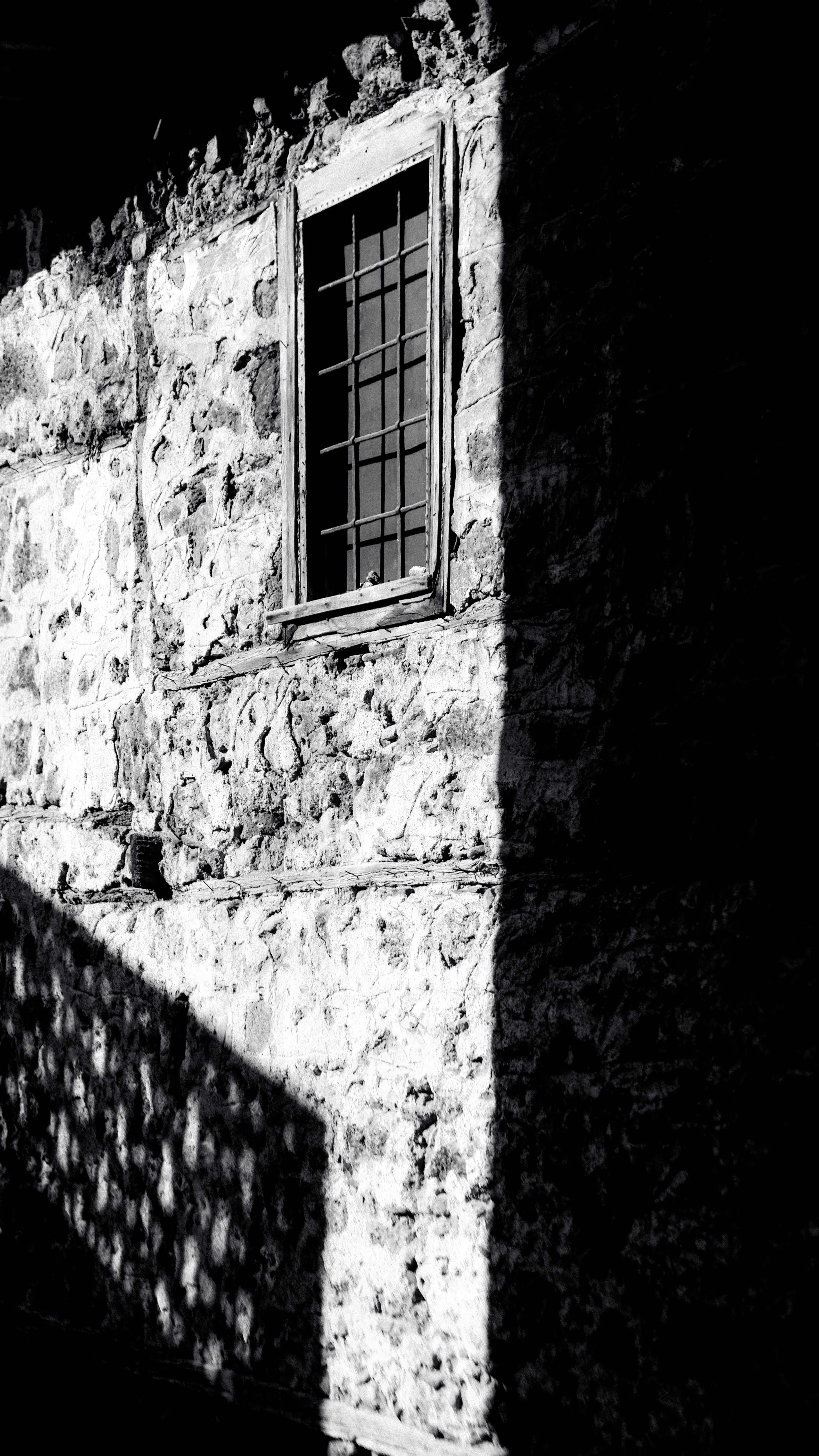High-contrast image of a stone building facade featuring a window with metal bars.