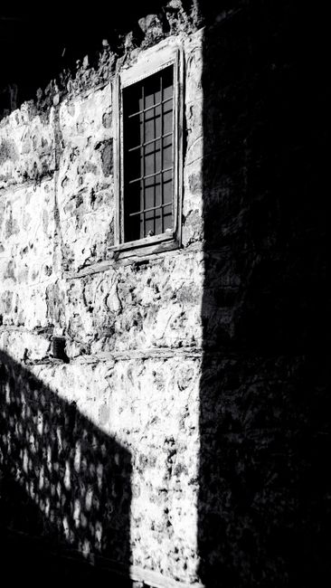 High-contrast image of a stone building facade featuring a window with metal bars.