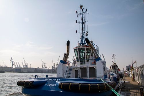 Free Tugboat docked at Hamburg port with industrial cranes in the distance, under a clear sky. Stock Photo