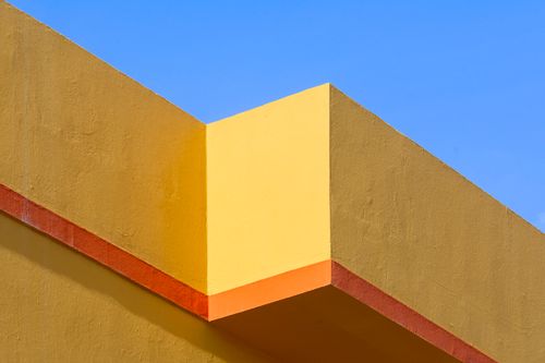 Free Vibrant architectural detail with yellow and orange hues contrasting a clear blue sky. Stock Photo