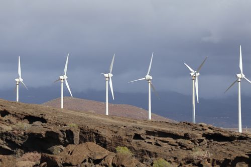 Free Line of wind turbines on rocky terrain beneath a cloudy sky, showcasing renewable energy. Stock Photo