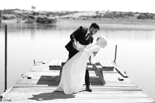 Free A couple in formal attire dances on a dock by a serene lake, exuding elegance and romance. Stock Photo