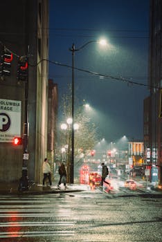Moody urban nightscape in Seattle with pedestrians crossing under rain-soaked streetlights.
