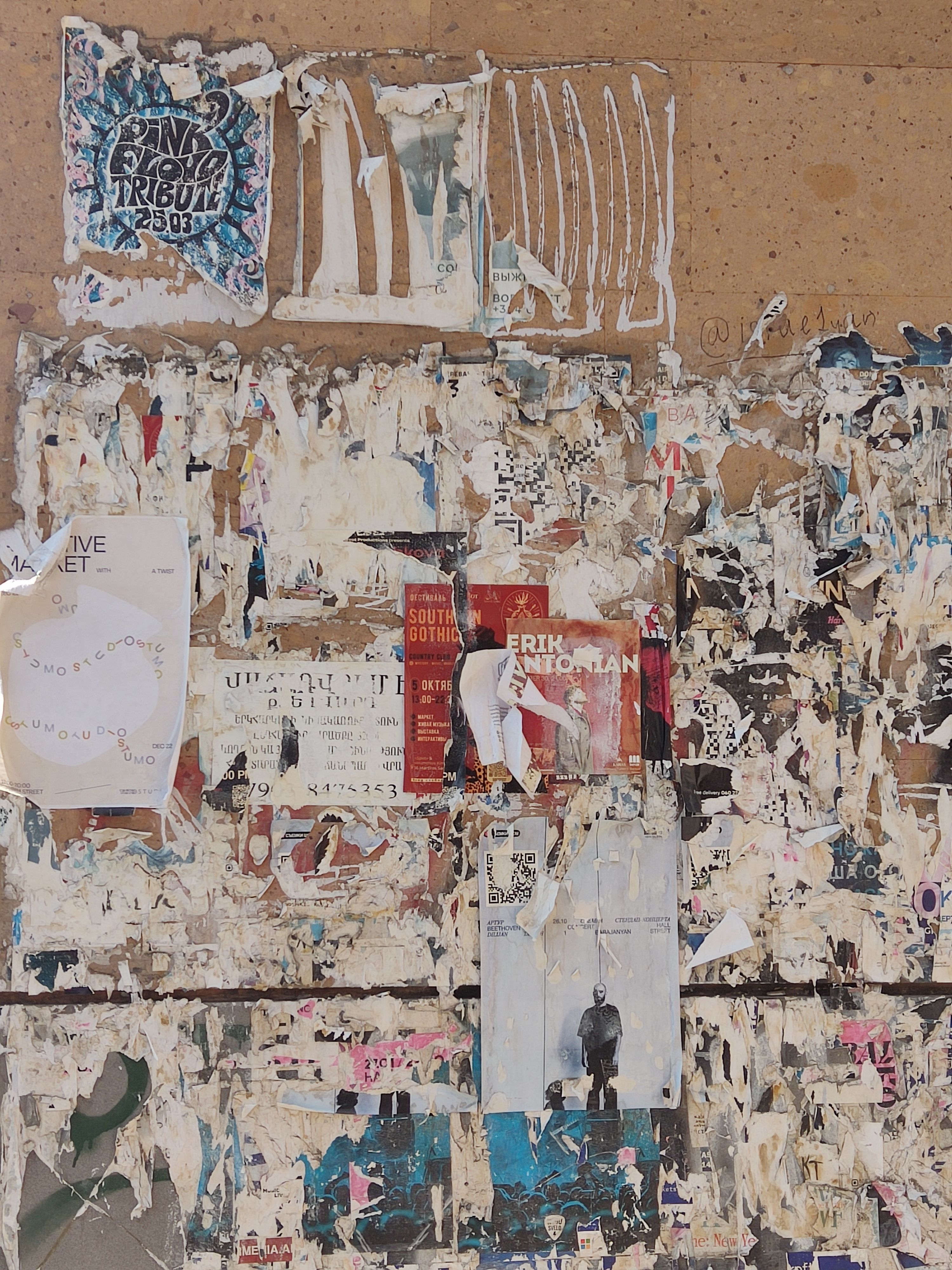Close-up of weathered bulletin board with torn and peeling posters.