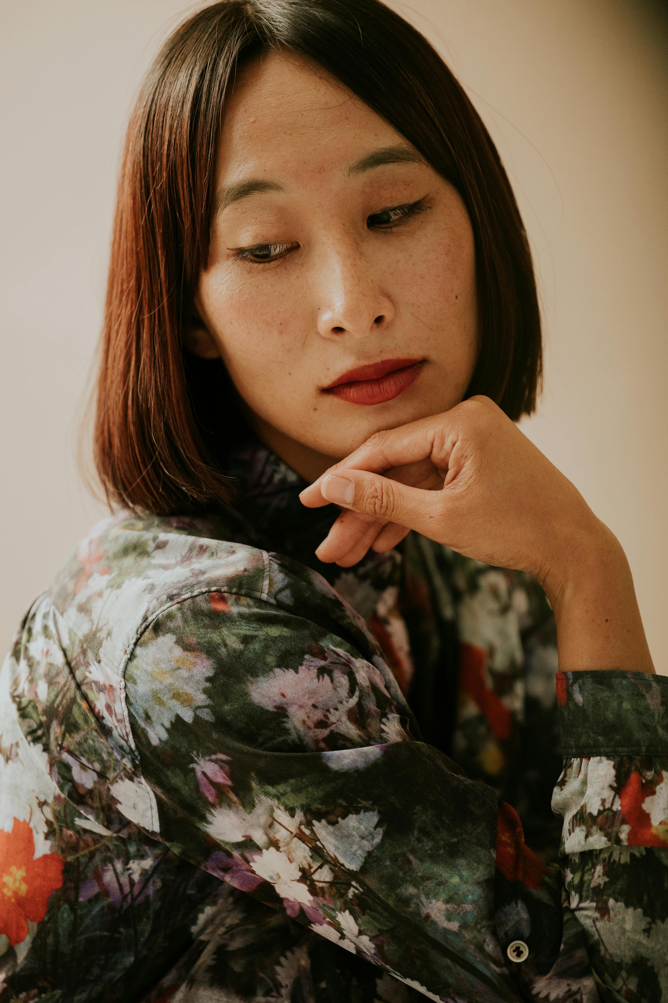 Woman in floral dress with thoughtful expression and artistic lighting.
