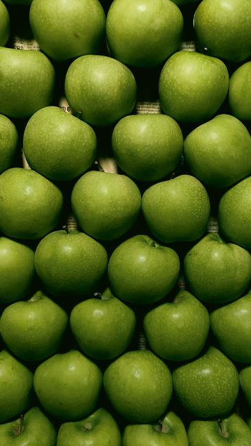 A golden-brown oat streusel topping over bubbling sliced Granny Smith apples in a white ceramic baking dish, with a scoop removed showing the tender apple filling underneath.