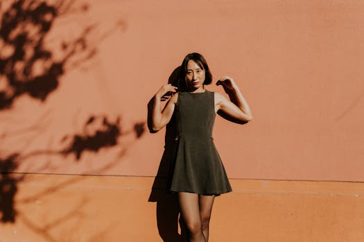 Stylish woman in a dress poses against a sunlit wall with artistic shadows.