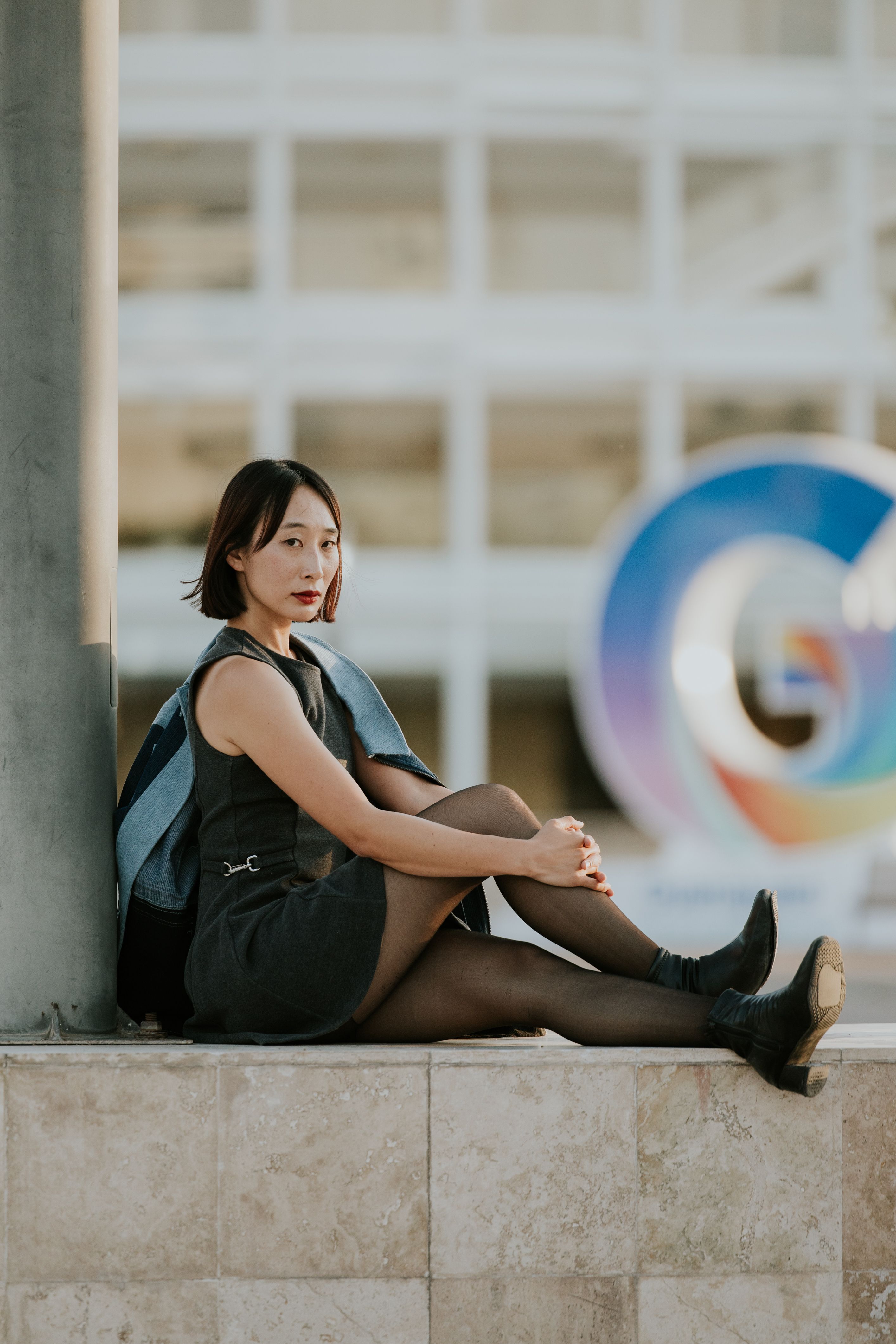 Stylish portrait of a young woman sitting outdoors against a colorful backdrop.